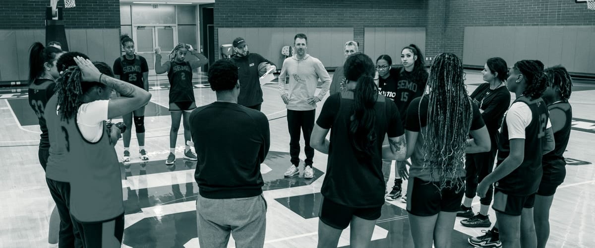 A coach with his team, gathered in a circle at practice